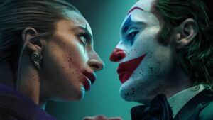 Joaquin Phoenix as Joker and Lady Gaga as Harley Quinn in an intense close-up scene from 'Joker: Folie à Deux,' with both characters wearing makeup and gazing at each other