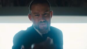 A focused man in a dark room illuminated by a soft overhead light, a dramatic scene from "Blink Twice."