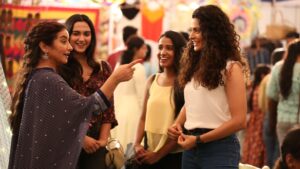  A joyful scene from Sharmajee Ki Beti showing a woman pointing and laughing with three young women in a bustling market.