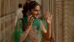 A still from 'Phir Aayi Hasseen Dillruba' showing a woman joyfully talking on the phone, dressed in a vibrant green saree, standing by a window with a smile, suggesting a light-hearted or emotional moment in the movie