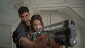 Two characters from Alien: Romulus preparing to fire a futuristic weapon.