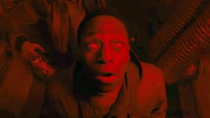 Character in Alien: Romulus experiencing a terrifying moment in red lighting.