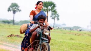 Thambi riding on a motorcycle with his teacher in the Tamil film Vaazhai, capturing their bond and village landscape.