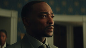 Sam Wilson, portrayed by Anthony Mackie, appears in a thoughtful moment from Captain America: Brave New World, wearing a suit and looking determined.