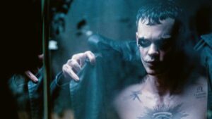 The Crow reveals his chest tattoos while staring intensely in The Crow 2024.